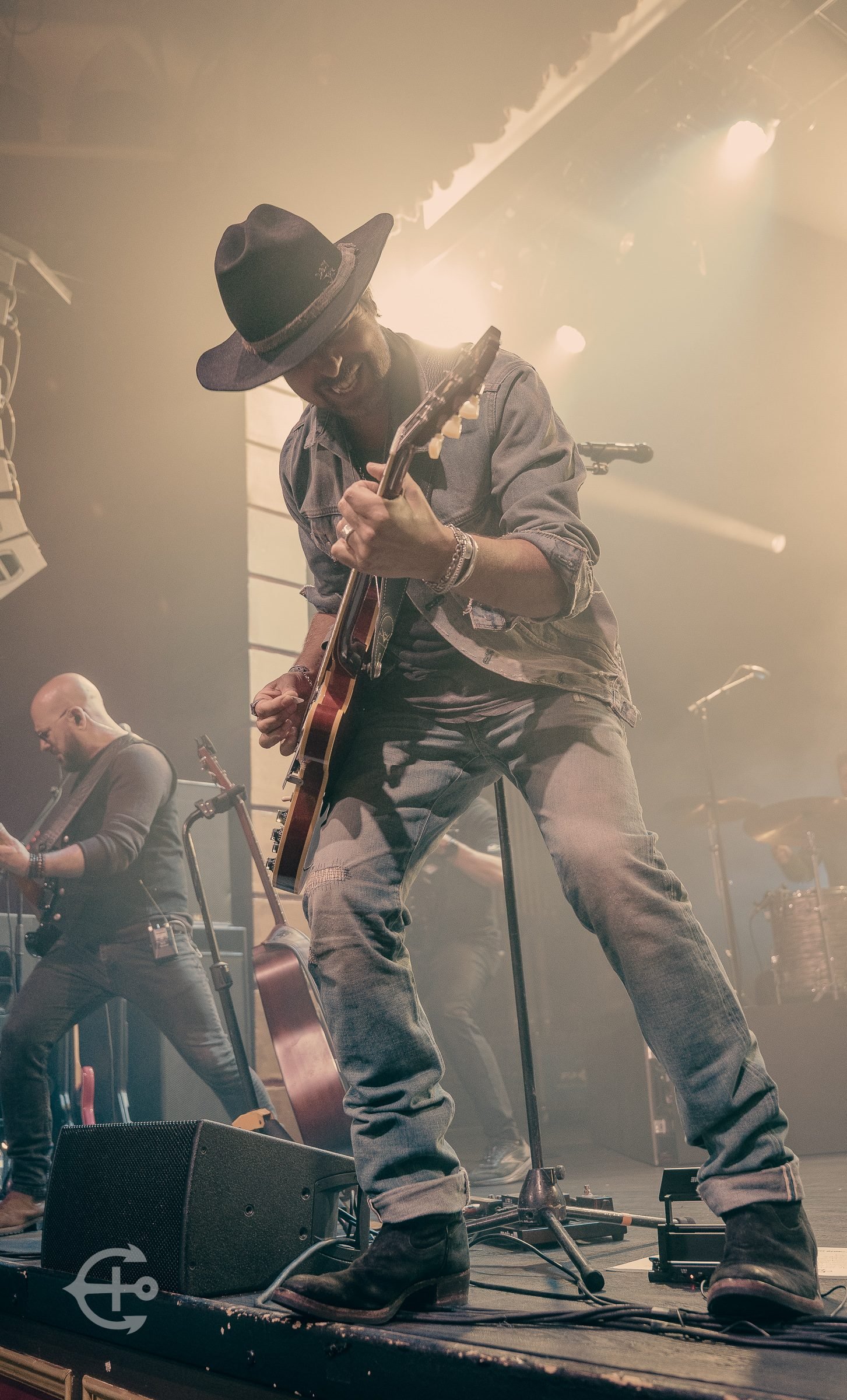 Guitarist in a wide-brim hat performing through stage haze