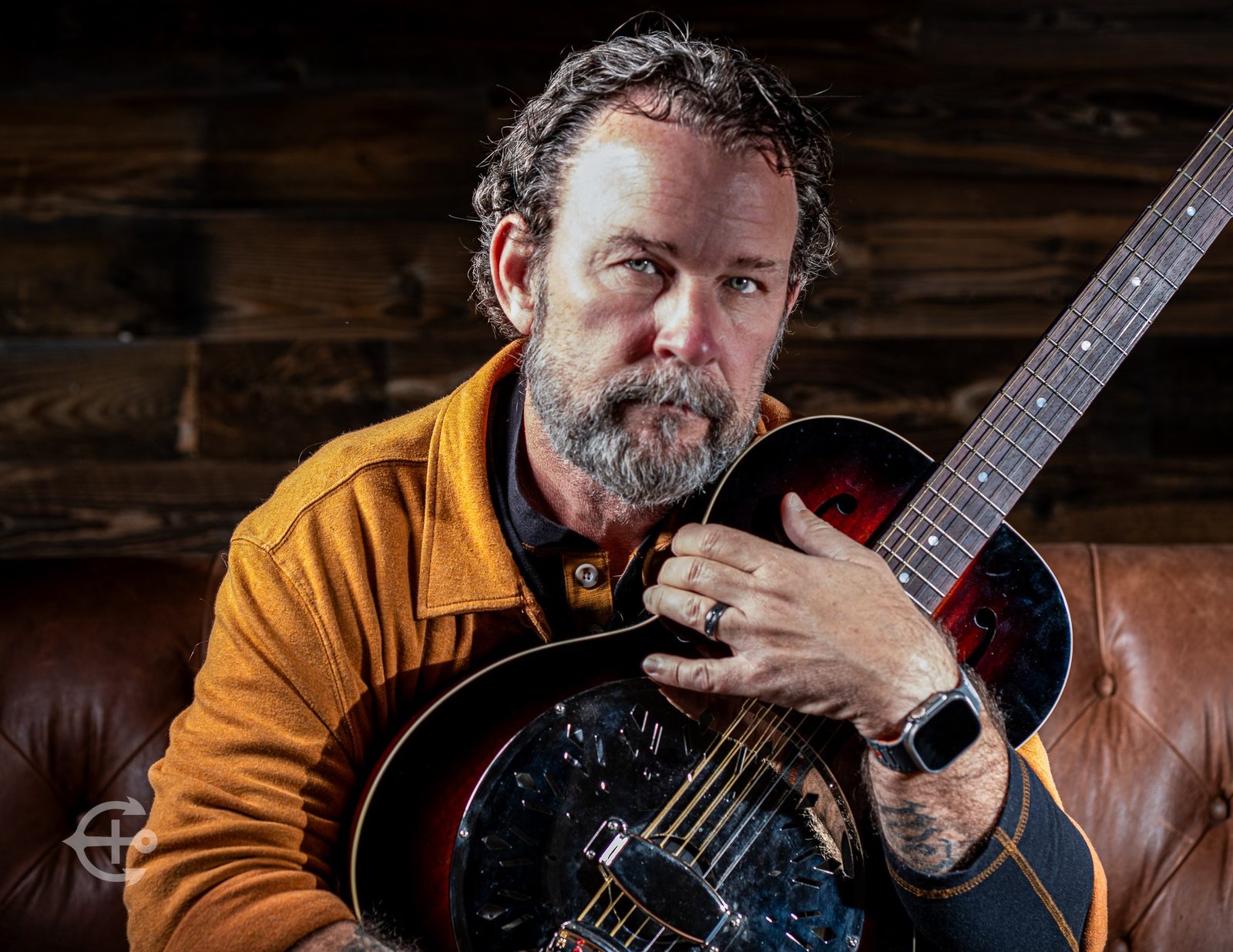 Musician seated with an electric guitar in a warm studio portrait