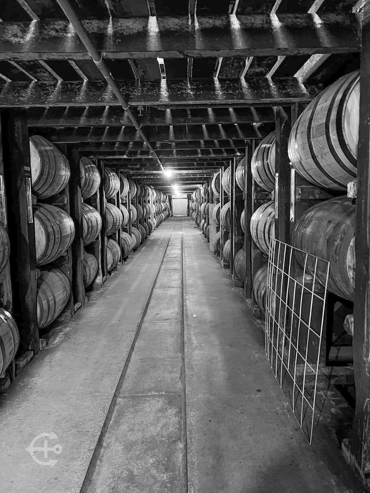 Black-and-white view down a warehouse aisle lined with barrels