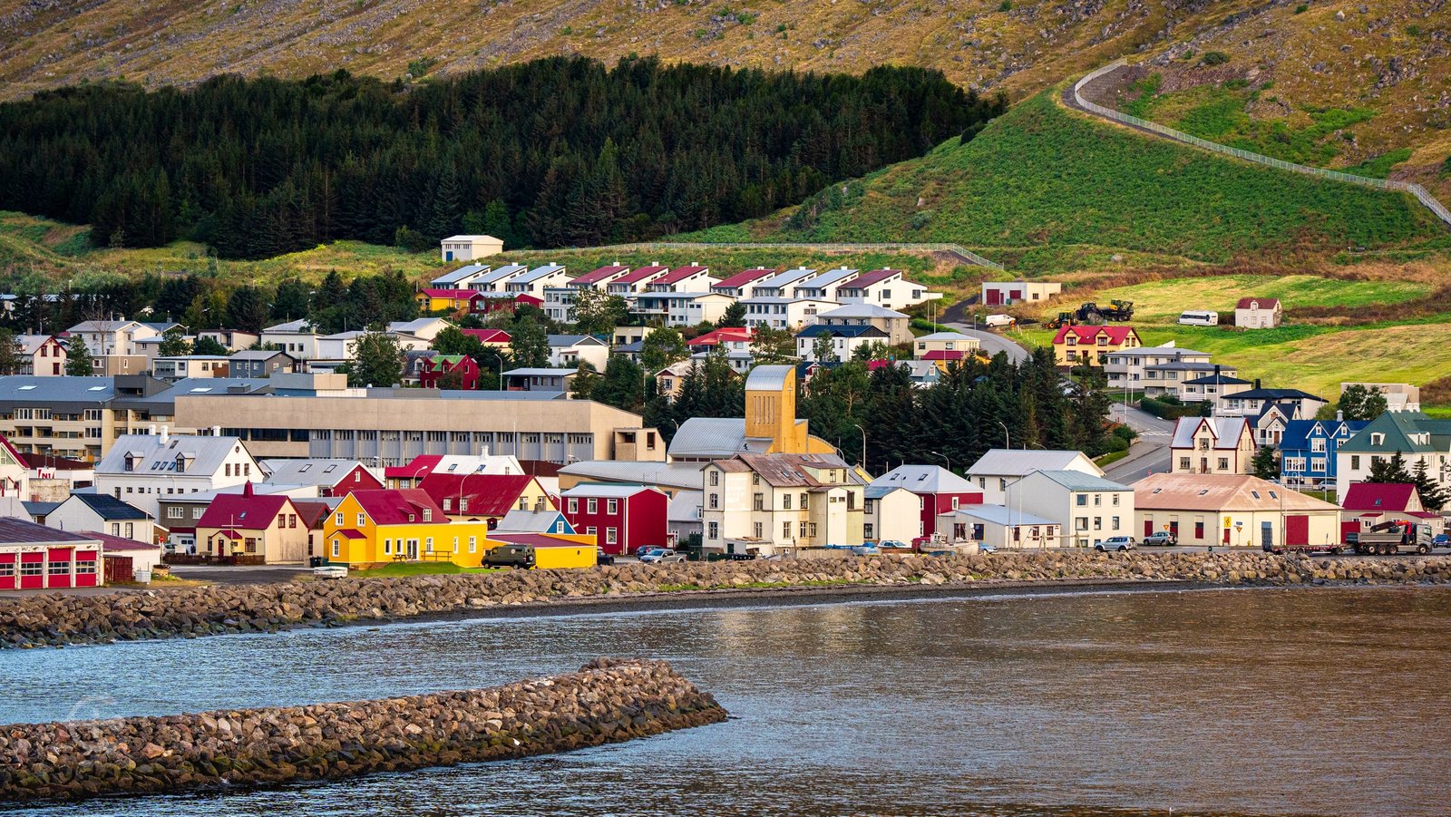 Colorful waterfront buildings and a church below a wooded hillside