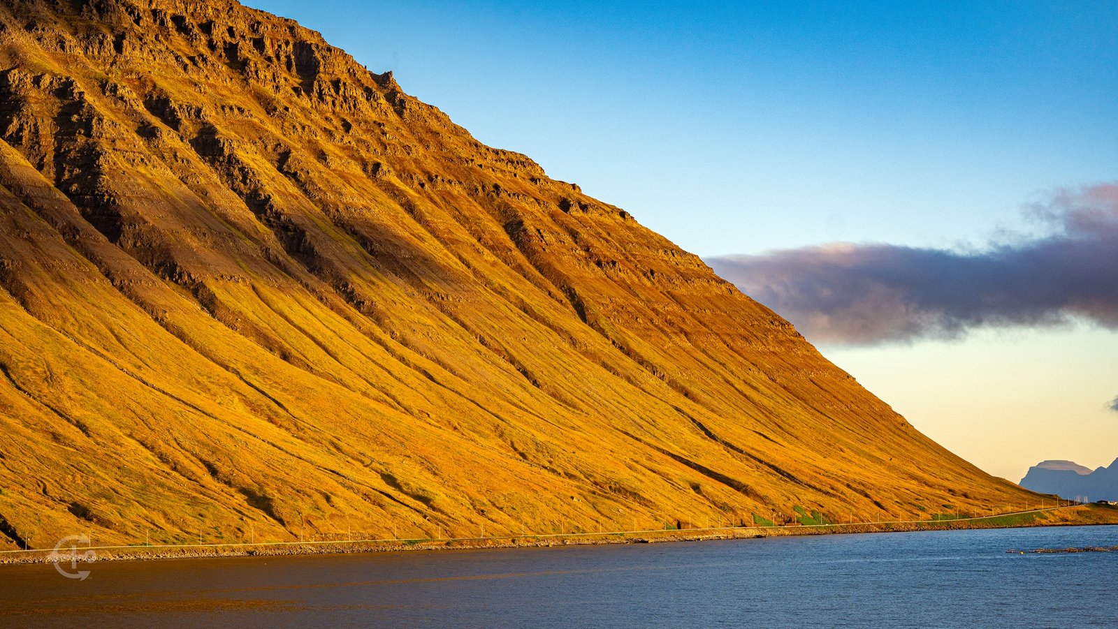 Golden light across a steep mountain slope beside the fjord