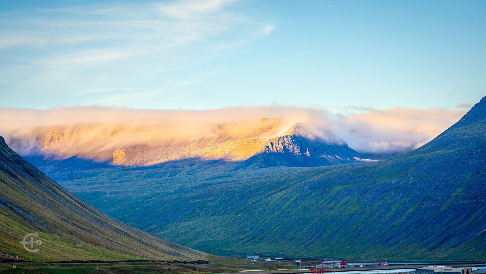 Warm sunlight and low cloud over the mountains surrounding the fjord