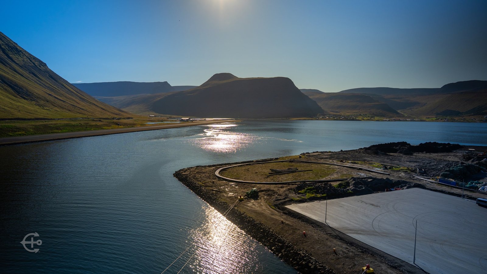 Sun reflected in the fjord beside a shoreline road and mountains