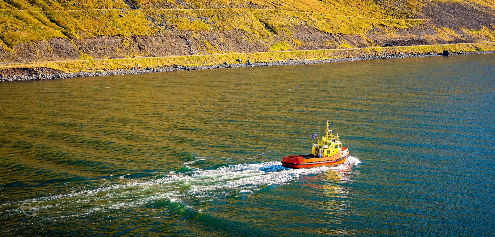 Red and yellow tugboat leaving a white wake beside the green shoreline
