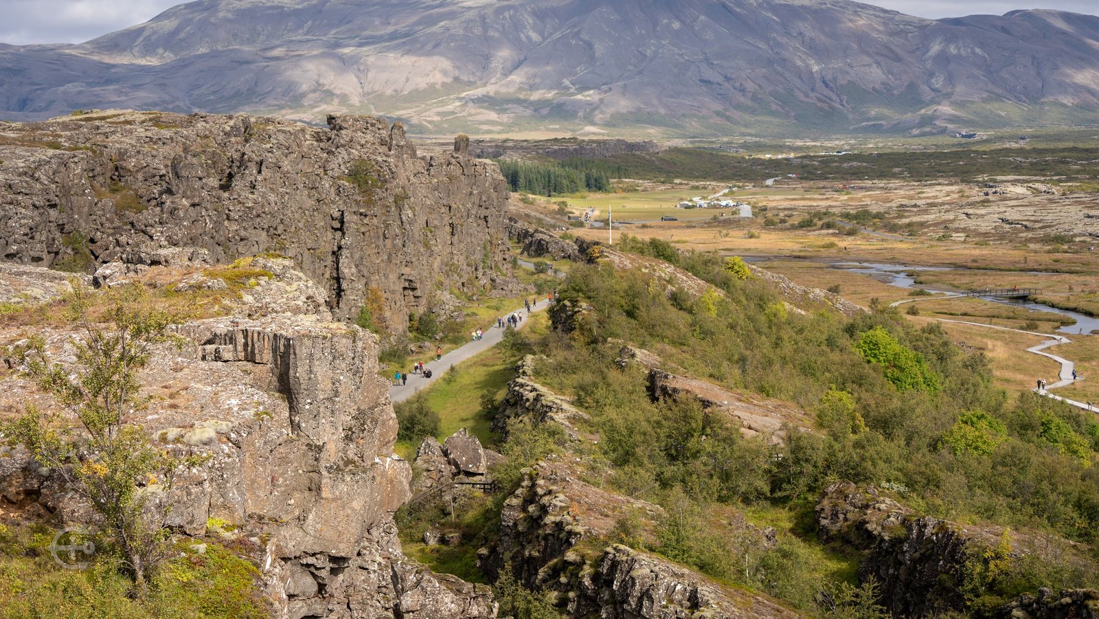 Walking path beneath a rocky escarpment with mountains across the valley