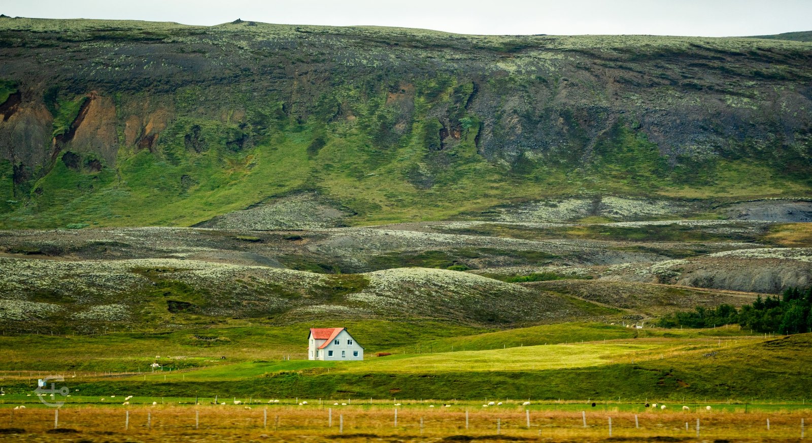 White farmhouse with a red roof beneath a green hillside
