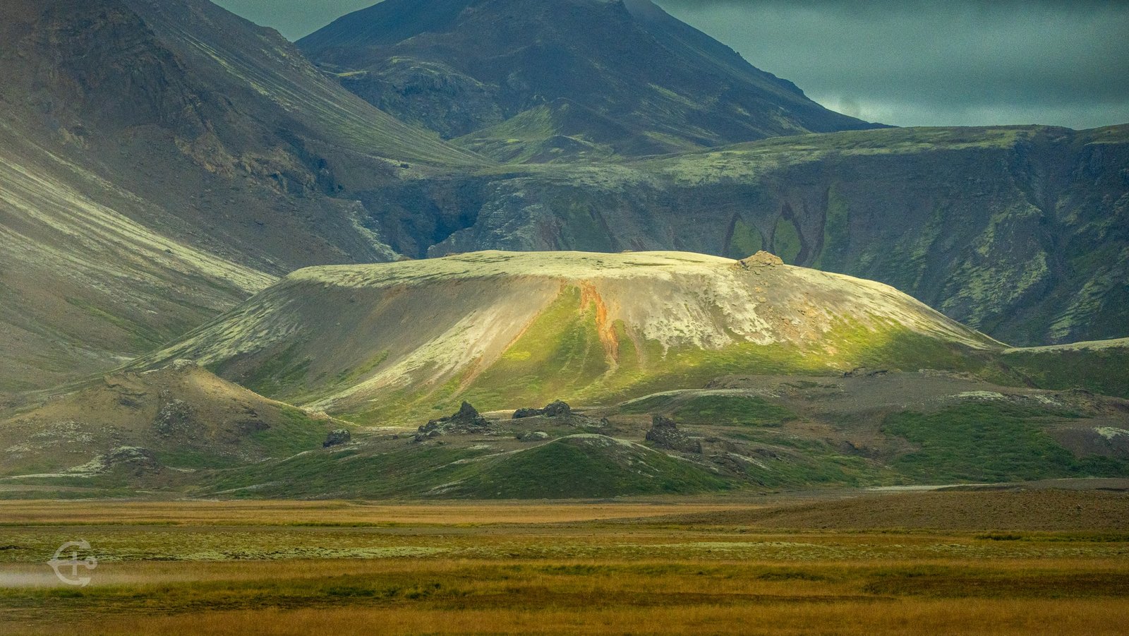Sunlight falling on a rounded hill surrounded by rugged mountains