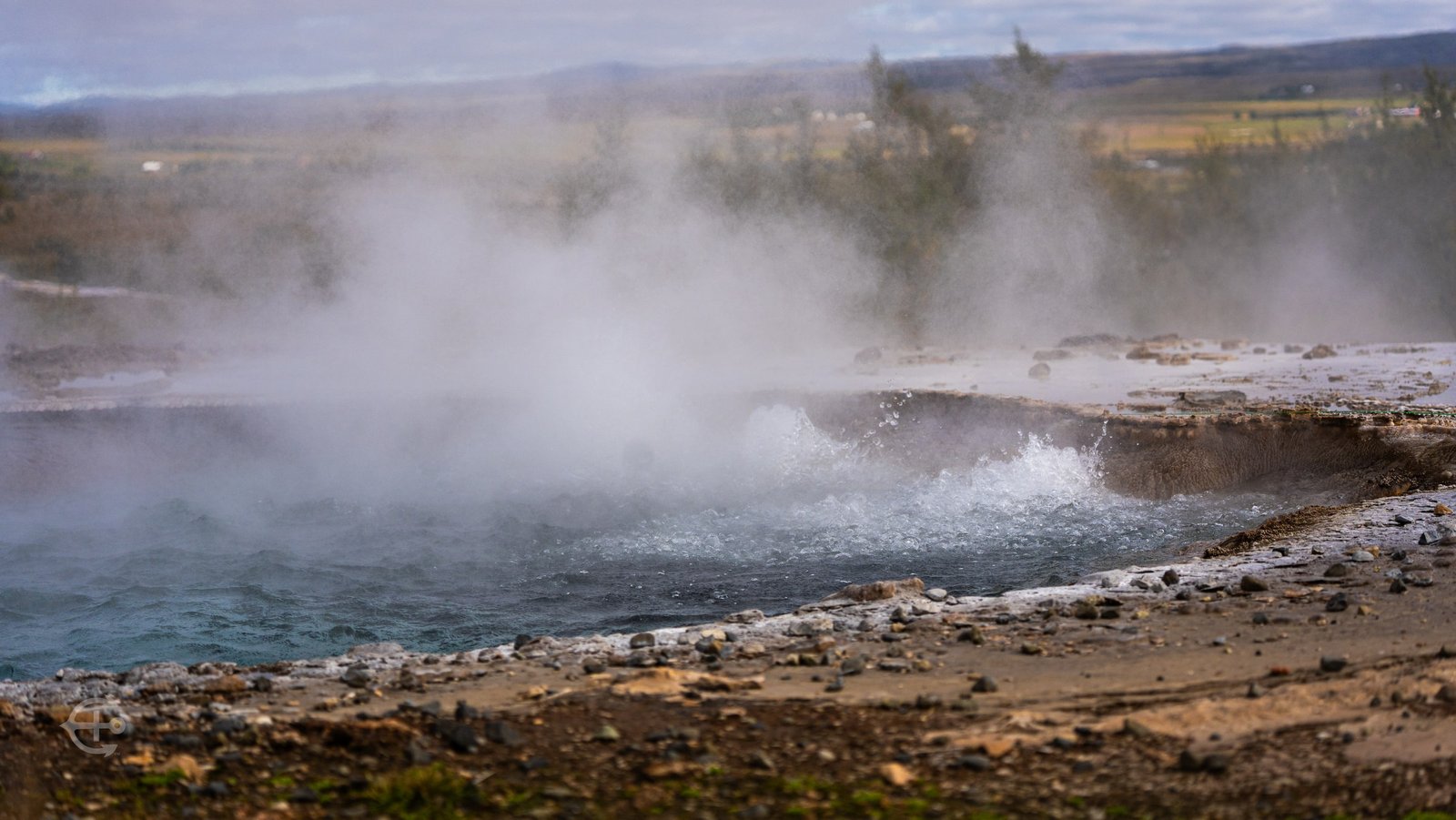 Steam rising above bubbling blue geothermal water