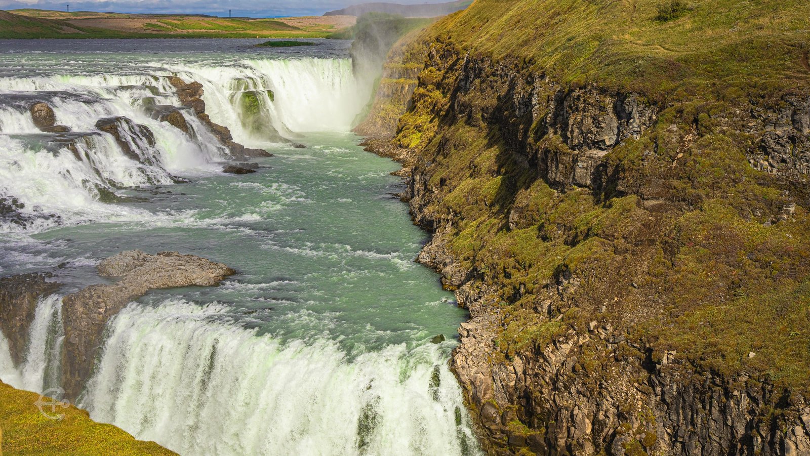 Water pouring over multiple tiers beside a steep canyon wall