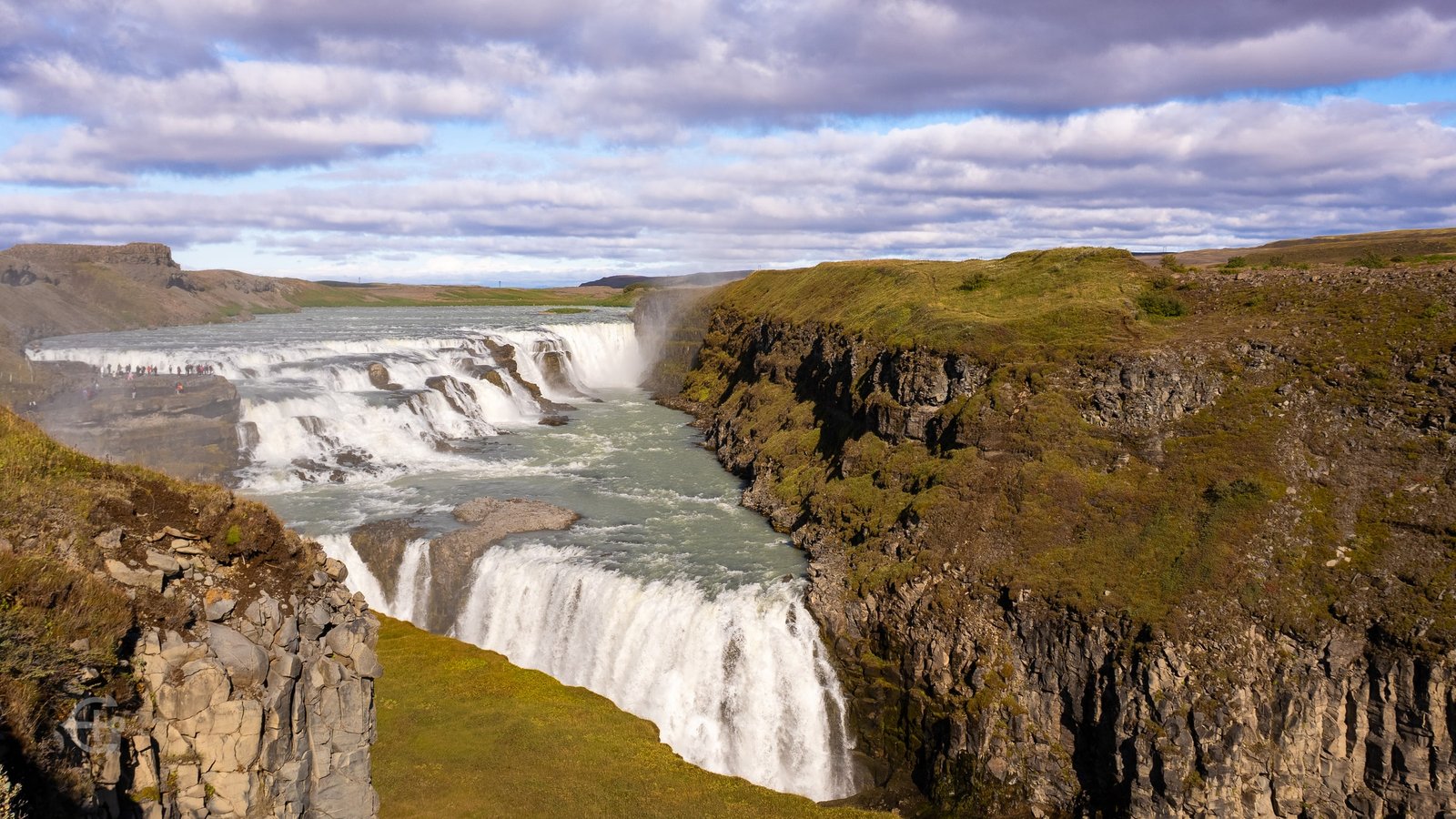 Broad waterfall cascading through a rocky canyon beneath a cloud-filled sky